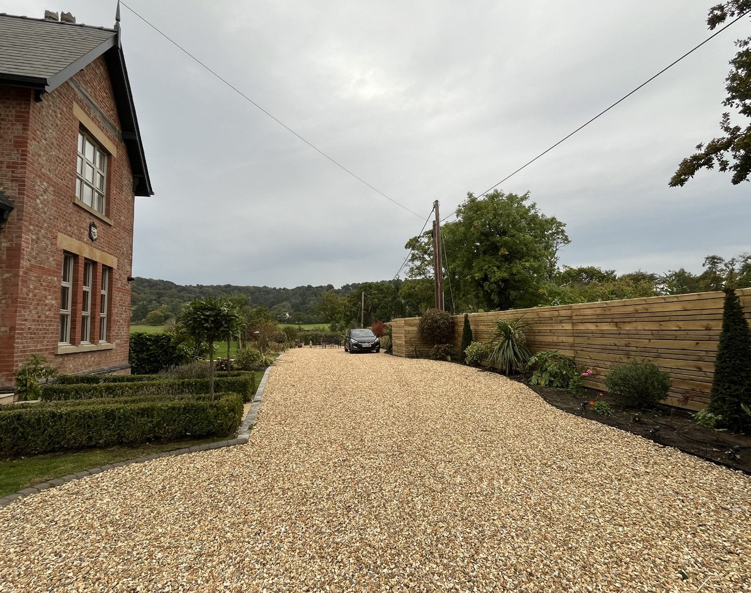 Completed gravel driveway curving past a brick house, edged with new hedging and lawn.