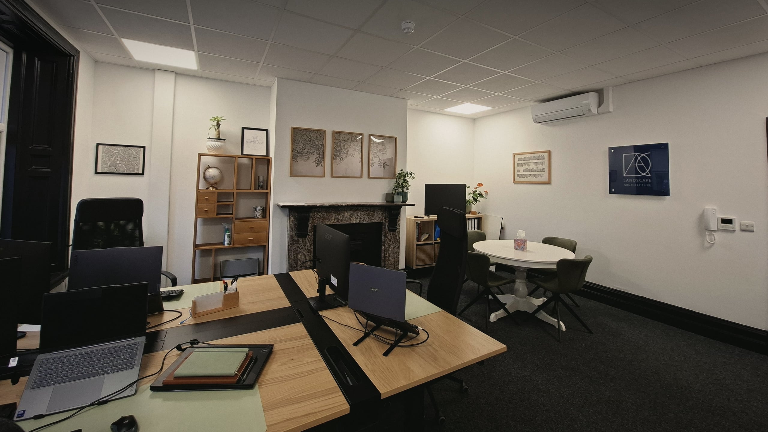 The DAC studio in Adlington: shared oak desks, a marble fireplace beneath three botanical prints, and the meeting table by the DAC Landscape Architecture sign.